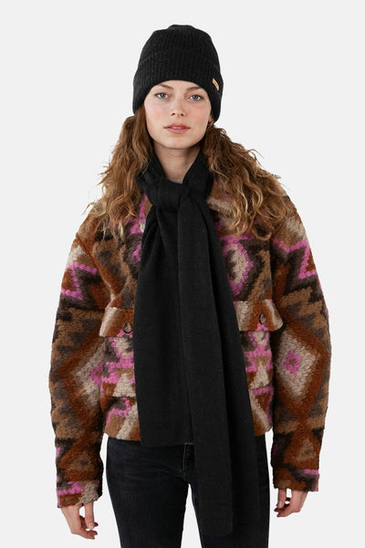 Écharpe noire de BARTS, nouée autour du cou, portée avec un bonnet noir et une veste à motifs géométriques.