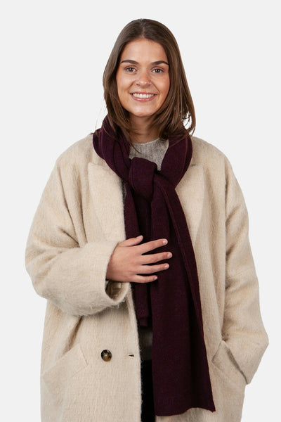 Écharpe rouge bordeaux de BARTS, nouée autour du cou, portée avec un manteau beige texturé.