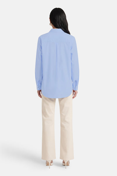 Chemise bleue à manches longues de Terra di Siena, vue de dos, portée avec un pantalon beige et des talons hauts.