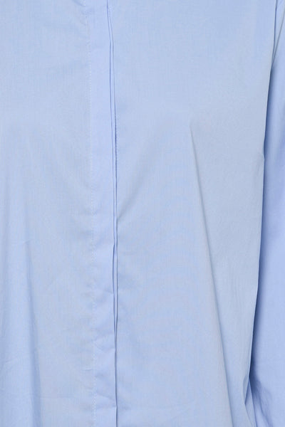 Chemisier bleu de Terra di Siena, avec patte de boutonnage et tissu uni légèrement froissé.