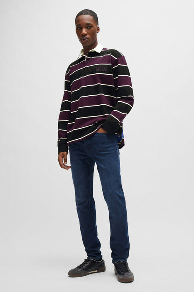 Jean fuselé en denim de BOSS ORANGE, porté avec un polo rayé et des chaussures de sport.
