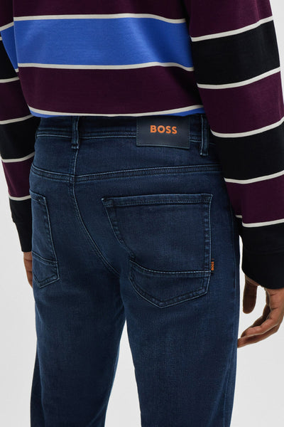 Jean fuselé bleu foncé de BOSS ORANGE, avec un pull rayé multicolore.