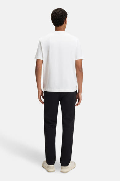 T-shirt à manches courtes blanc de BOSS ORANGE, porté avec un pantalon noir et des baskets beiges, vue de dos.
