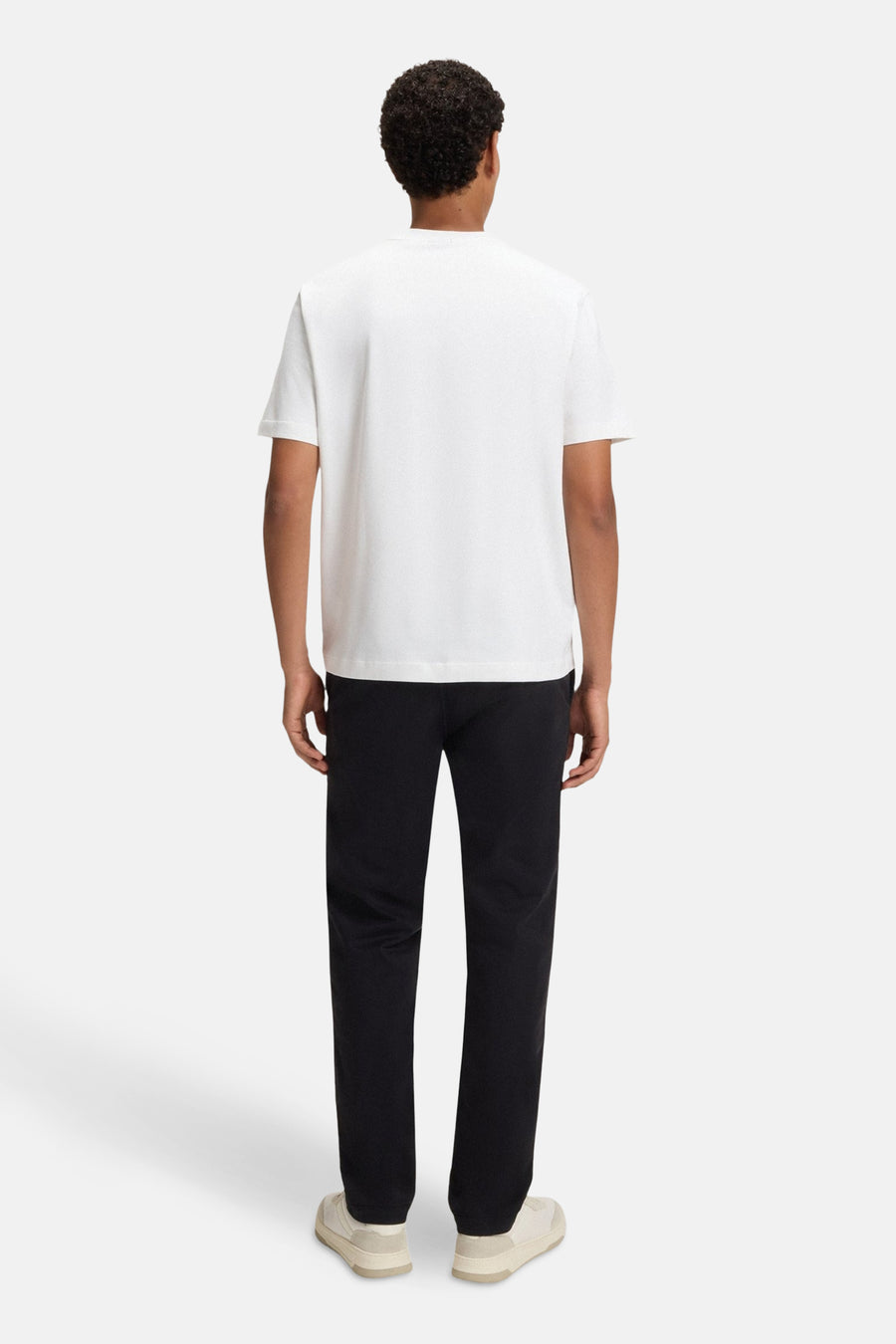 T-shirt à manches courtes blanc de BOSS ORANGE, porté avec un pantalon noir et des baskets beiges, vue de dos.