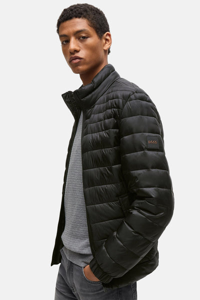 Veste courte grise de BOSS ORANGE, avec matelassage horizontal et fermeture éclair, portée avec un pull gris et un jean.