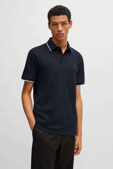 Polo bleu marine de BOSS ORANGE, avec des bordures blanches au col et aux manches, porté avec un pantalon noir.
