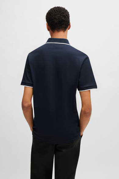 Polo bleu marine par BOSS ORANGE, avec bordures blanches au col et aux manches, porté avec un pantalon noir, vue de dos.

