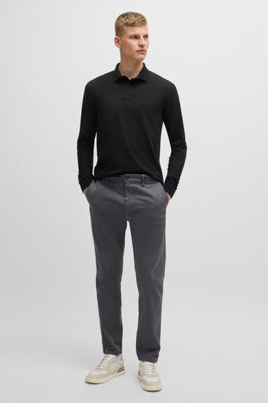 Zwart poloshirt met lange mouwen van BOSS ORANGE, gedragen met een grijze broek en crèmekleurige sportschoenen.