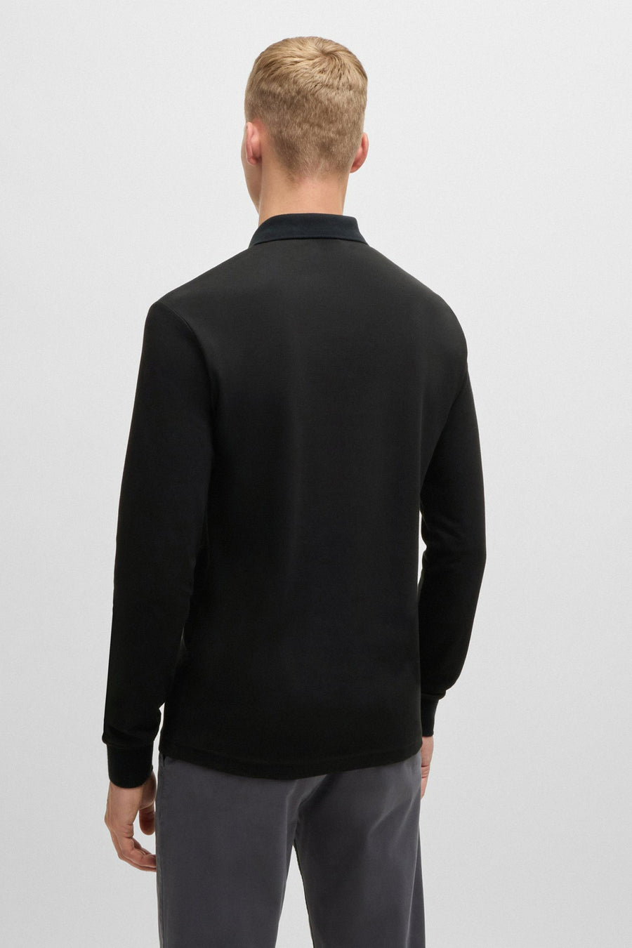 Zwarte polo met lange mouwen van BOSS ORANGE, gedragen met een antracietgrijze broek, achtergezicht.