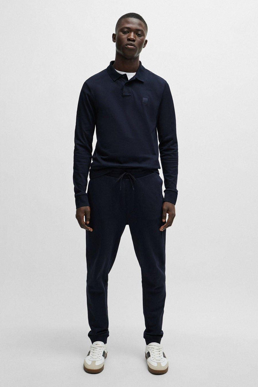 Polo bleu marine de BOSS ORANGE, porté avec un pantalon de jogging et des chaussures de sport blanches.