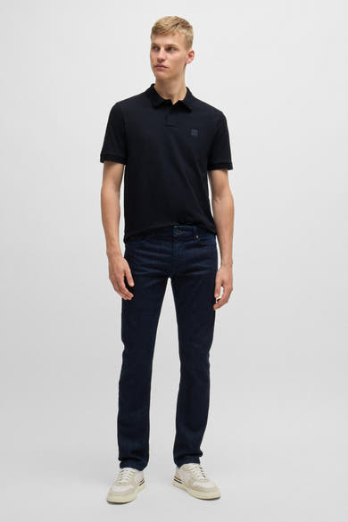 Polo bleu à manches courtes de BOSS ORANGE, porté avec un jean bleu foncé et des baskets beiges.