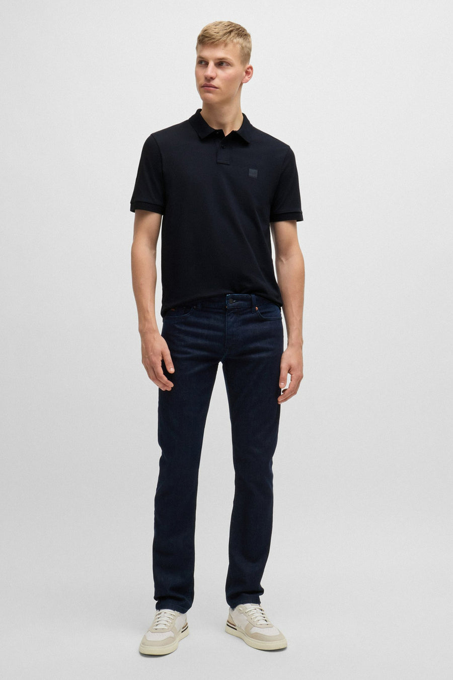 Polo bleu à manches courtes de BOSS ORANGE, porté avec un jean bleu foncé et des baskets beiges.