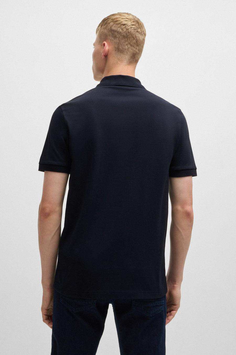 Polo bleu à manches courtes de BOSS ORANGE, porté avec un pantalon en jean bleu foncé, vue de dos.