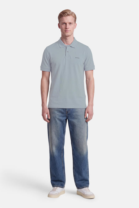 Polo gris à manches courtes de BOSS ORANGE, col boutonné, logo discret sur poitrine, porté avec jeans délavés et baskets blanches, vue frontale.