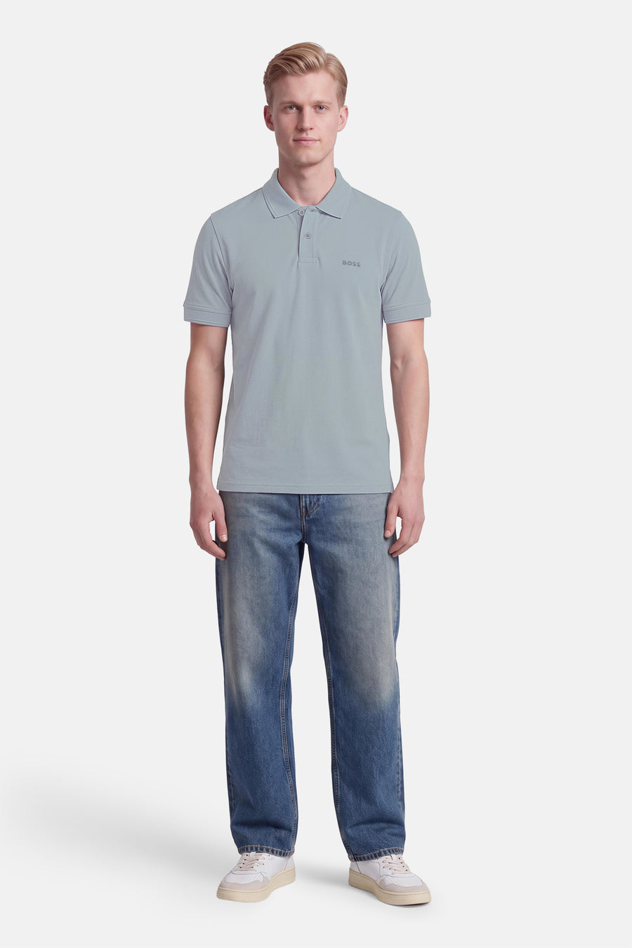 Polo gris à manches courtes de BOSS ORANGE, col boutonné, logo discret sur poitrine, porté avec jeans délavés et baskets blanches, vue frontale.