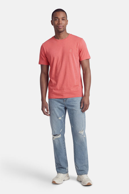 Roze T-shirt met korte mouwen van BOSS ORANGE met een reliëf logo-patch op de borst, gedragen met een gescheurde spijkerbroek en lichte sneakers.