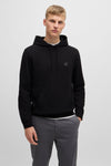 Sweat à capuche noir de BOSS ORANGE, avec cordon de serrage et poche kangourou, porté sur un pantalon gris.
