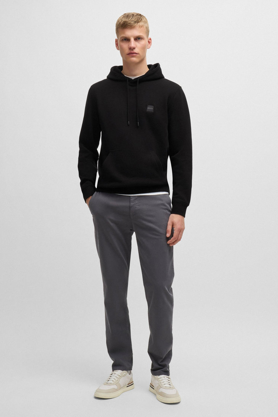 Sweat à capuche noir de BOSS ORANGE, porté avec un pantalon gris et des baskets beiges.
