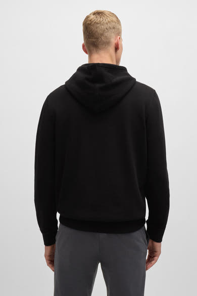 Sweat à capuche noir de BOSS Orange, vue de dos, porté avec un pantalon gris.
