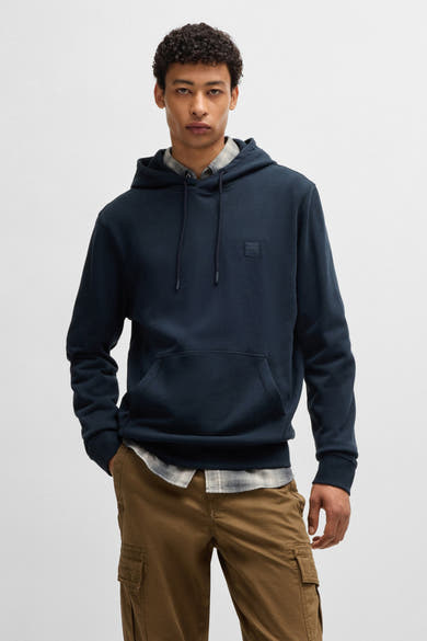 Blauwe hoodie van BOSS ORANGE, gedragen over een geruit overhemd en een bruine cargobroek.