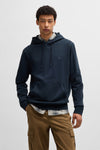 Blauwe hoodie van BOSS ORANGE, gedragen over een geruit overhemd en een bruine cargobroek.