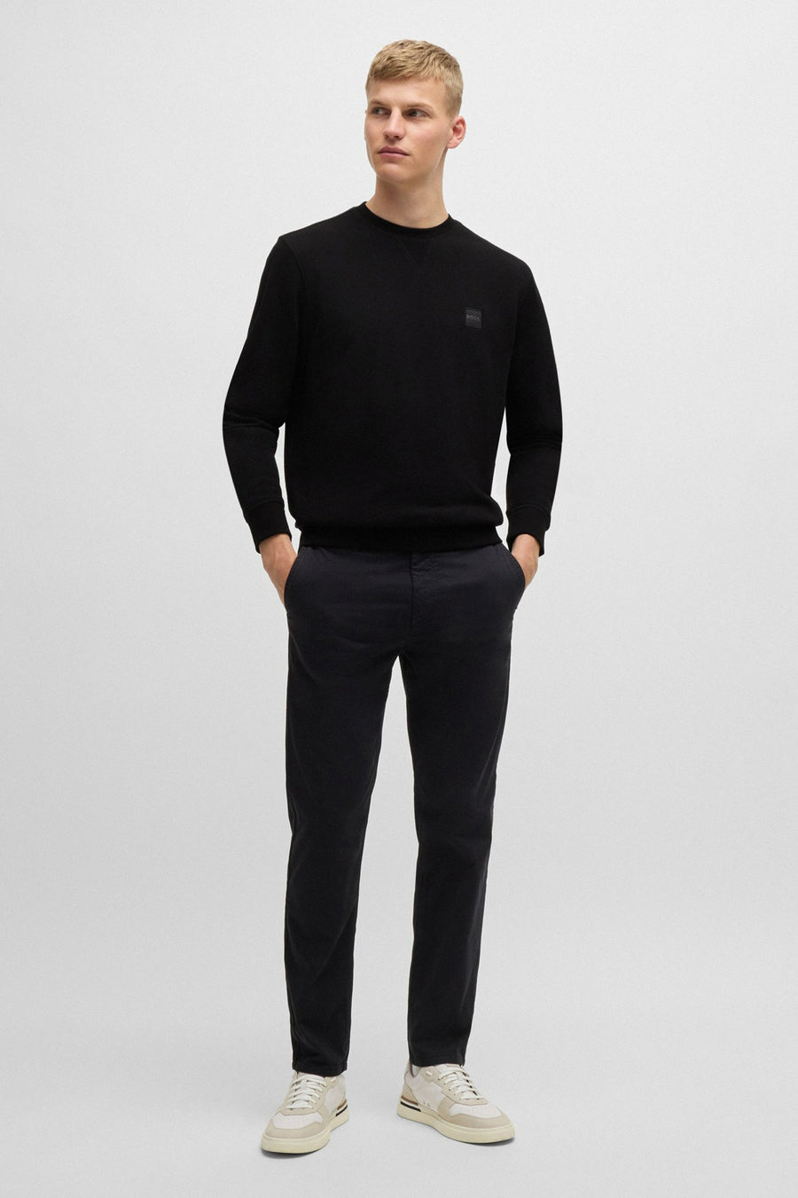 Sweat noir de BOSS ORANGE, porté avec un pantalon foncé et des chaussures de sport crème.
