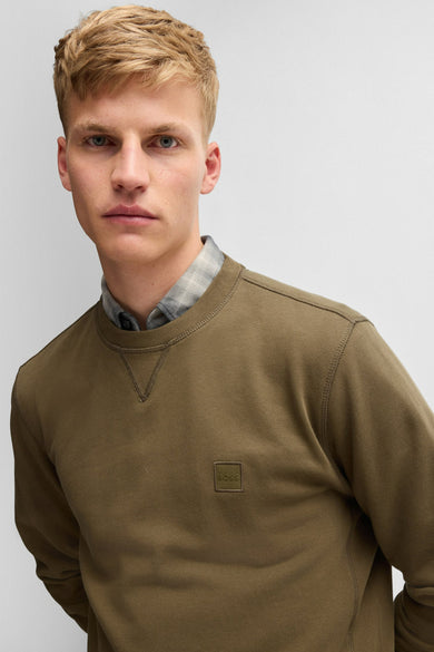 Sweat-shirt kaki de BOSS ORANGE, porté sur une chemise à carreaux discrets.