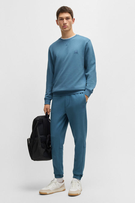 Blauwe rondehals sweatshirt van BOSS ORANGE, gedragen met een joggingbroek en een zwarte rugzak.