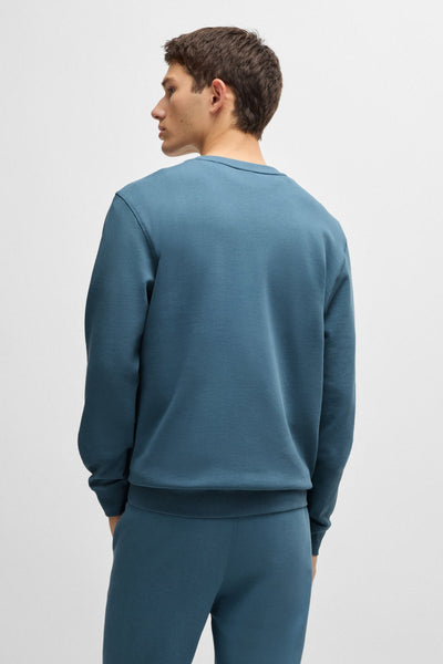 Sweat col rond bleu de BOSS ORANGE, modèle uni vu de dos porté avec un pantalon assorti.