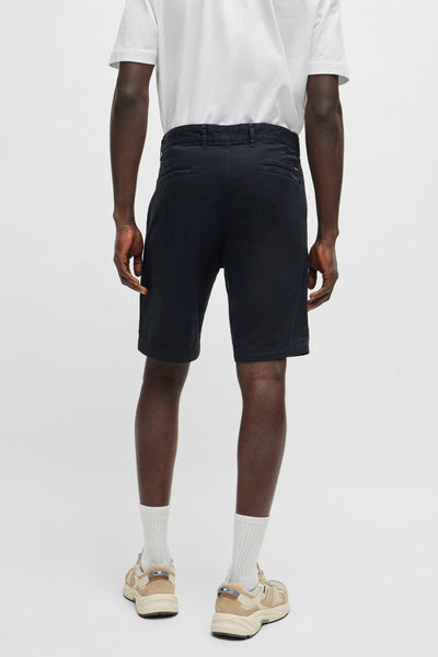 Bermuda bleu de BOSS ORANGE, porté avec un t-shirt blanc et des chaussures de sport beiges, vue de dos.