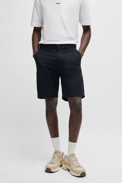 Bermuda bleu de BOSS ORANGE porté avec un t-shirt blanc et des baskets couleur sable.
