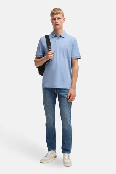 Polo bleu par BOSS ORANGE, porté avec un jean bleu et des chaussures de sport écrus, avec un sac à dos noir.