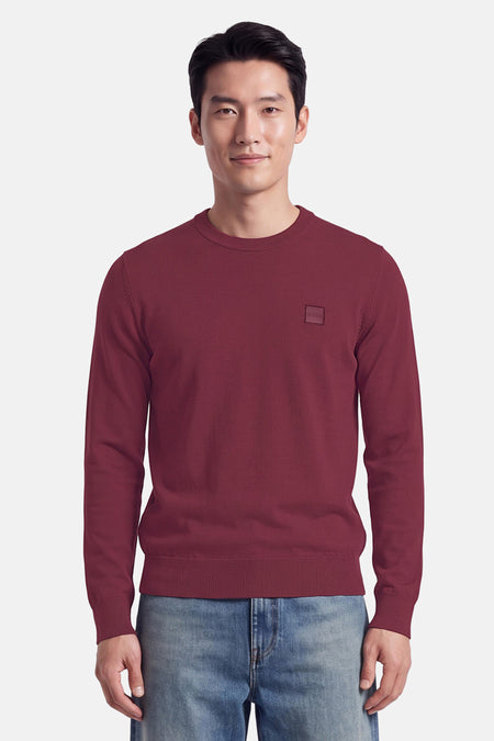 Pull col rond rouge de BOSS ORANGE, coupe ajustée, détail logo discret sur poitrine, porté avec jeans délavés, vue frontale.