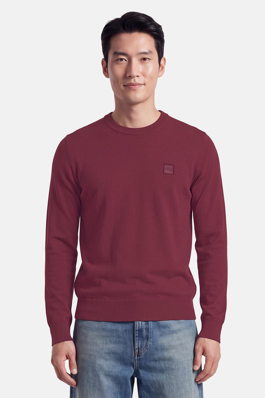 Pull col rond rouge de BOSS ORANGE, coupe ajustée, détail logo discret sur poitrine, porté avec jeans délavés, vue frontale.