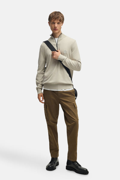 Beige coltrui van BOSS ORANGE, gedragen met een wit T-shirt, een bruine cargobroek en zwarte laarzen.