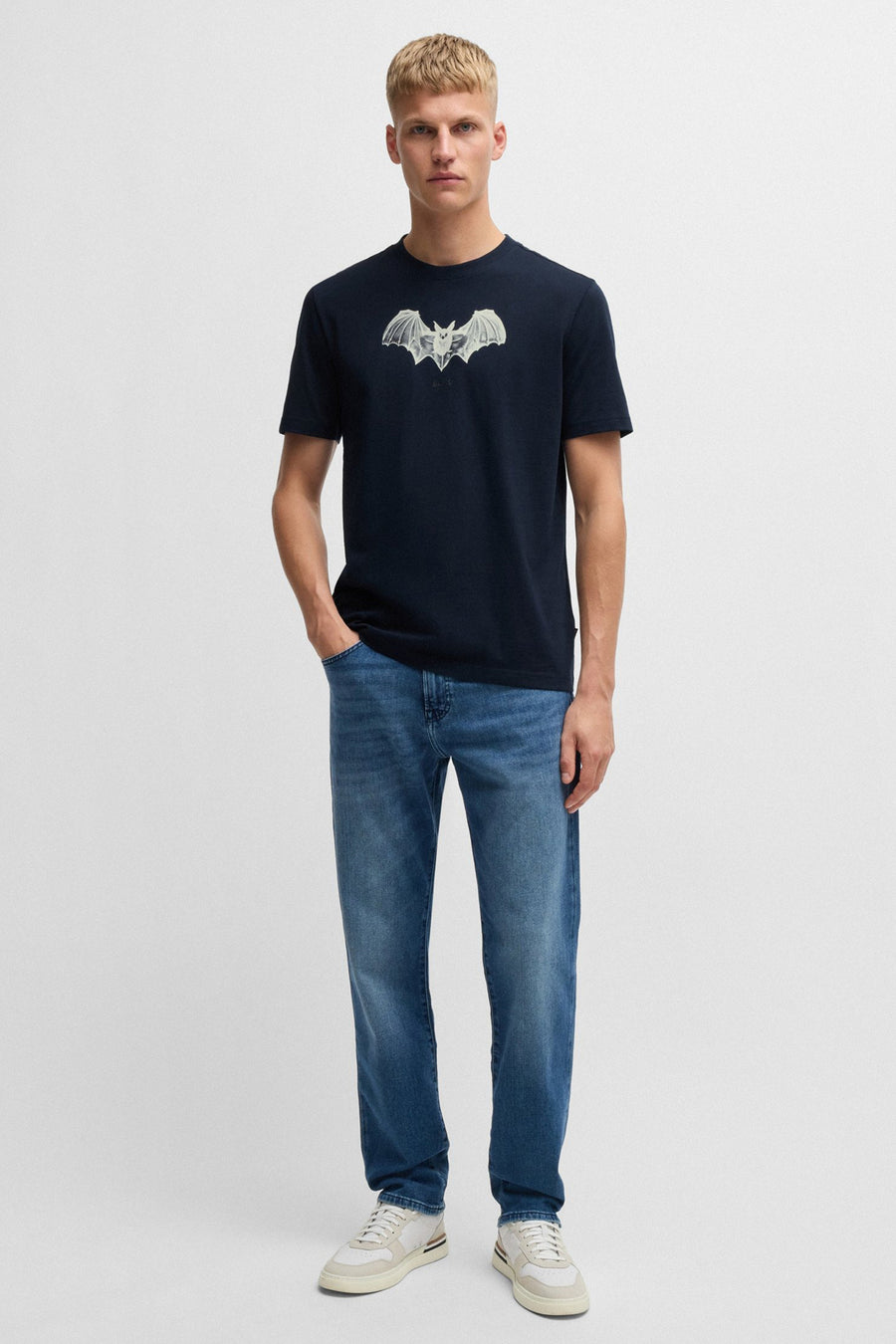 Blauw T-shirt met korte mouwen van BOSS ORANGE, met een vleermuisprint op de voorkant, gedragen met een spijkerbroek en sneakers.