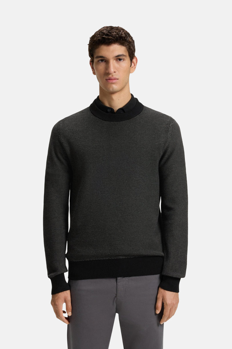 Zwarte trui met ronde hals van BOSS ORANGE, met een getextureerd patroon, gedragen over een zwart overhemd en een grijze broek.