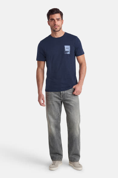 T-shirt à manches courtes bleu par BOSS ORANGE, avec un motif carré sur la poitrine, porté avec un jean gris et des baskets.
