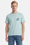 T-shirt turquoise de BOSS ORANGE avec motif rectangulaire de feuilles de palmier et 7.8 sur la poitrine, porté par un homme.