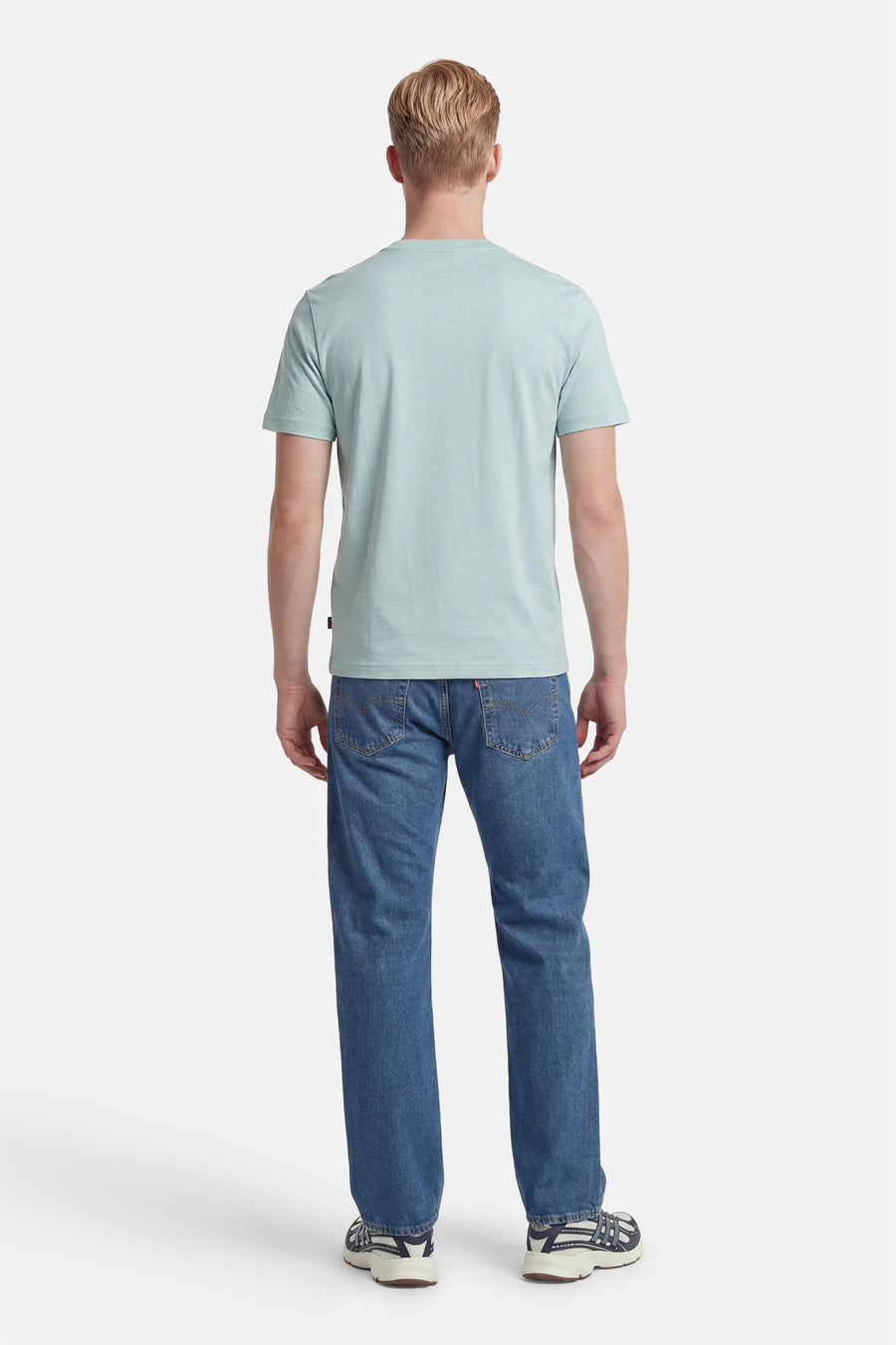 T-shirt turquoise de BOSS ORANGE porté par un homme de dos, associé à un jean bleu et des baskets.