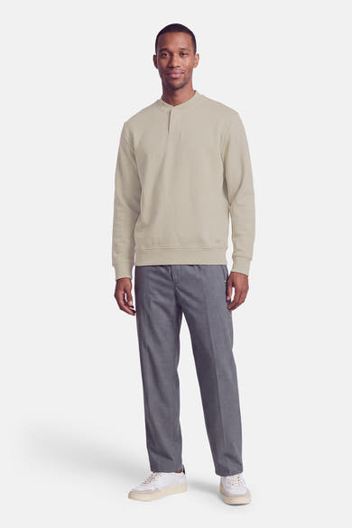 Sweat à col roulant beige de BOSS ORANGE, coupe droite, manches longues, avec détail de poche discrète sur le devant, porté avec pantalon gris et baskets blanches, vue frontale.