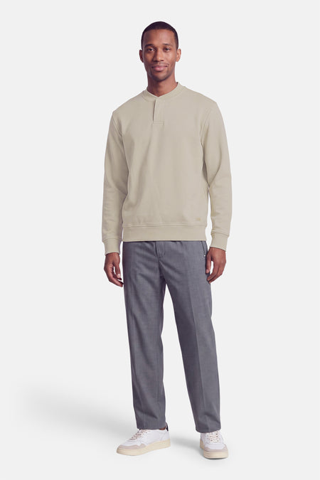 Sweat à col roulant beige de BOSS ORANGE, coupe droite, manches longues, avec détail de poche discrète sur le devant, porté avec pantalon gris et baskets blanches, vue frontale.