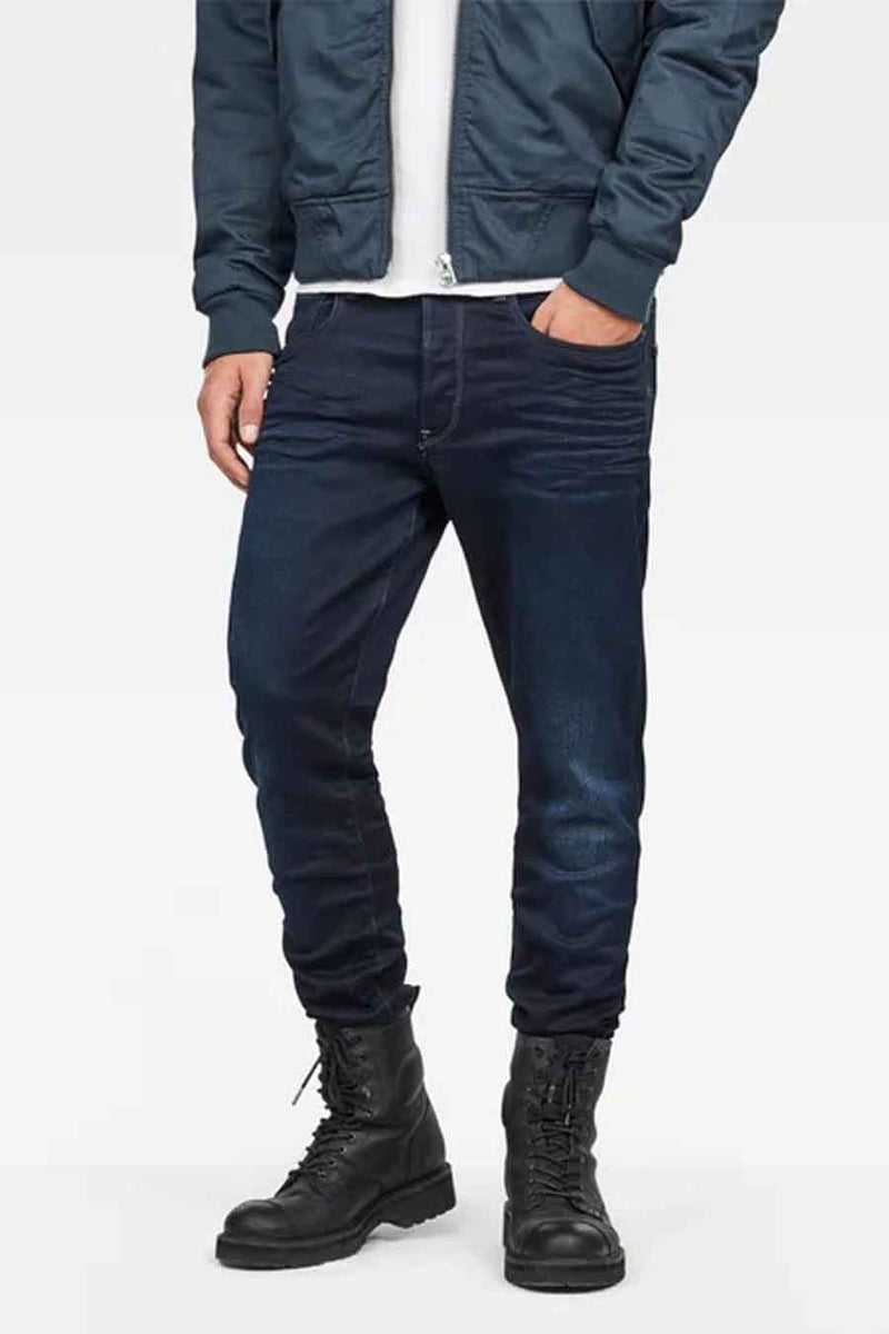 Blauwe slim fit jeans van G-Star RAW, met donkere wassing en kenmerkende achterzakken, gedragen met een blauwe trui.