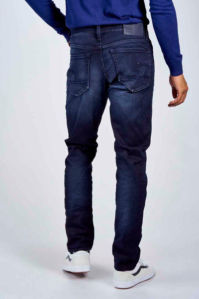 Jean slim bleu par G-Star RAW, avec délavage foncé et poches arrière distinctives, porté avec un pull bleu.