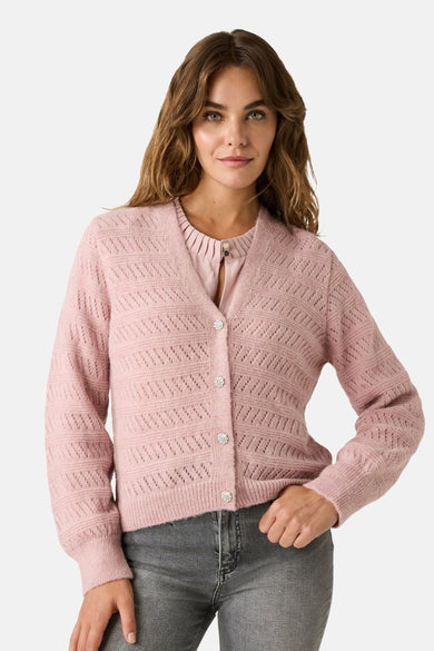 Roze gebreid vest met open structuur van MORE & MORE, gedragen met een roze T-shirt, grijze jeans en roze sneakers.