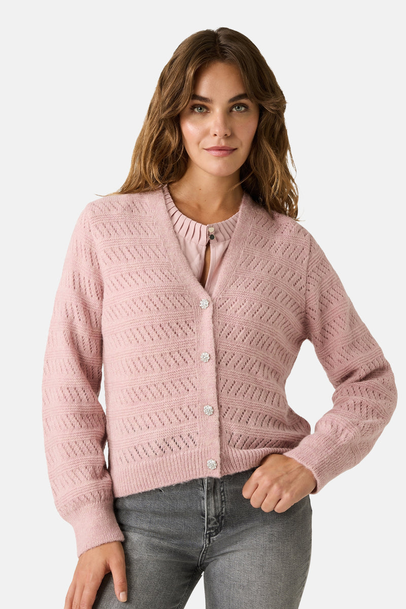 Roze gebreid vest met open structuur van MORE & MORE, gedragen met een roze T-shirt, grijze jeans en roze sneakers.