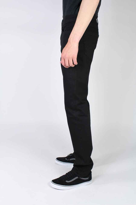 Jeans slim noirs en denim par Levi's®, vue de profil, ajustés, avec t-shirt noir et baskets noires à semelles blanches