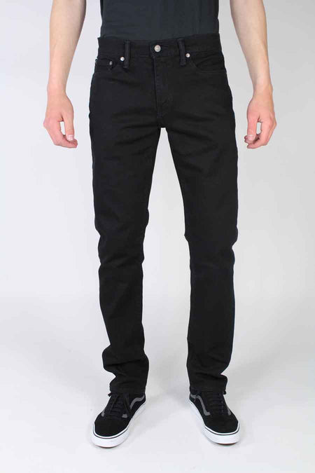 Jeans slim noirs en denim par Levi's® portés avec un t-shirt noir et des sneakers, vue de face
