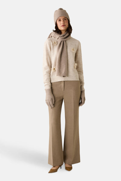 Pull à col rond beige de MORE & MORE, orné de fleurs décoratives, porté avec un pantalon marron, un bonnet et une écharpe assortis.