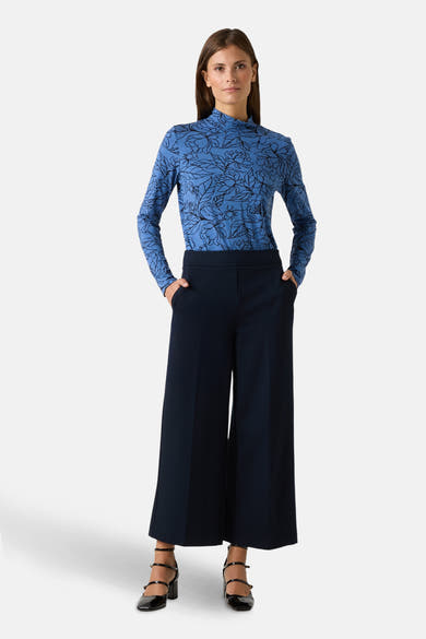 T-shirt à manches longues bleu, de MORE & MORE, avec motif floral noir, porté avec un pantalon large marine et des chaussures à talons.
